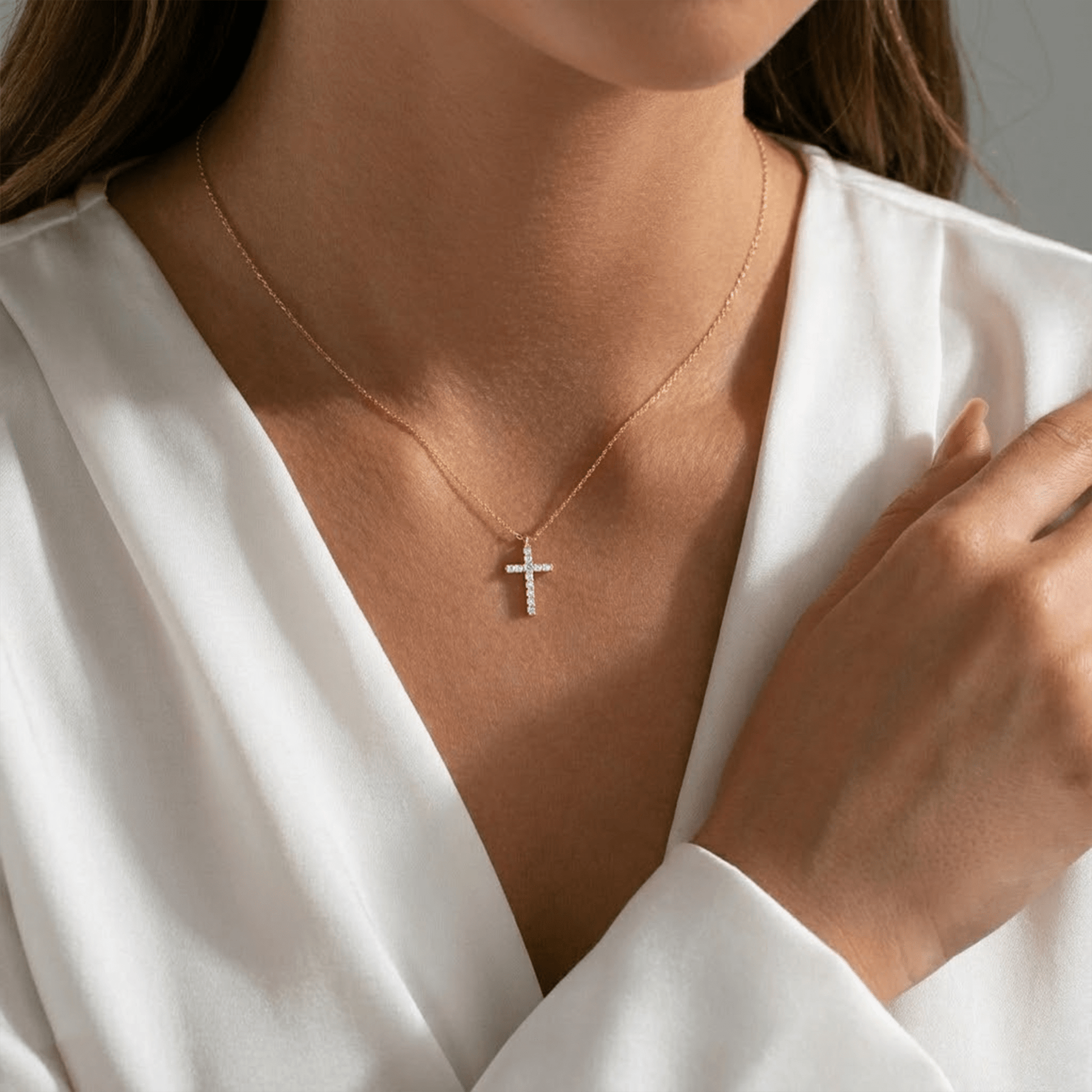 Person wearing a gold cross necklace with a white top