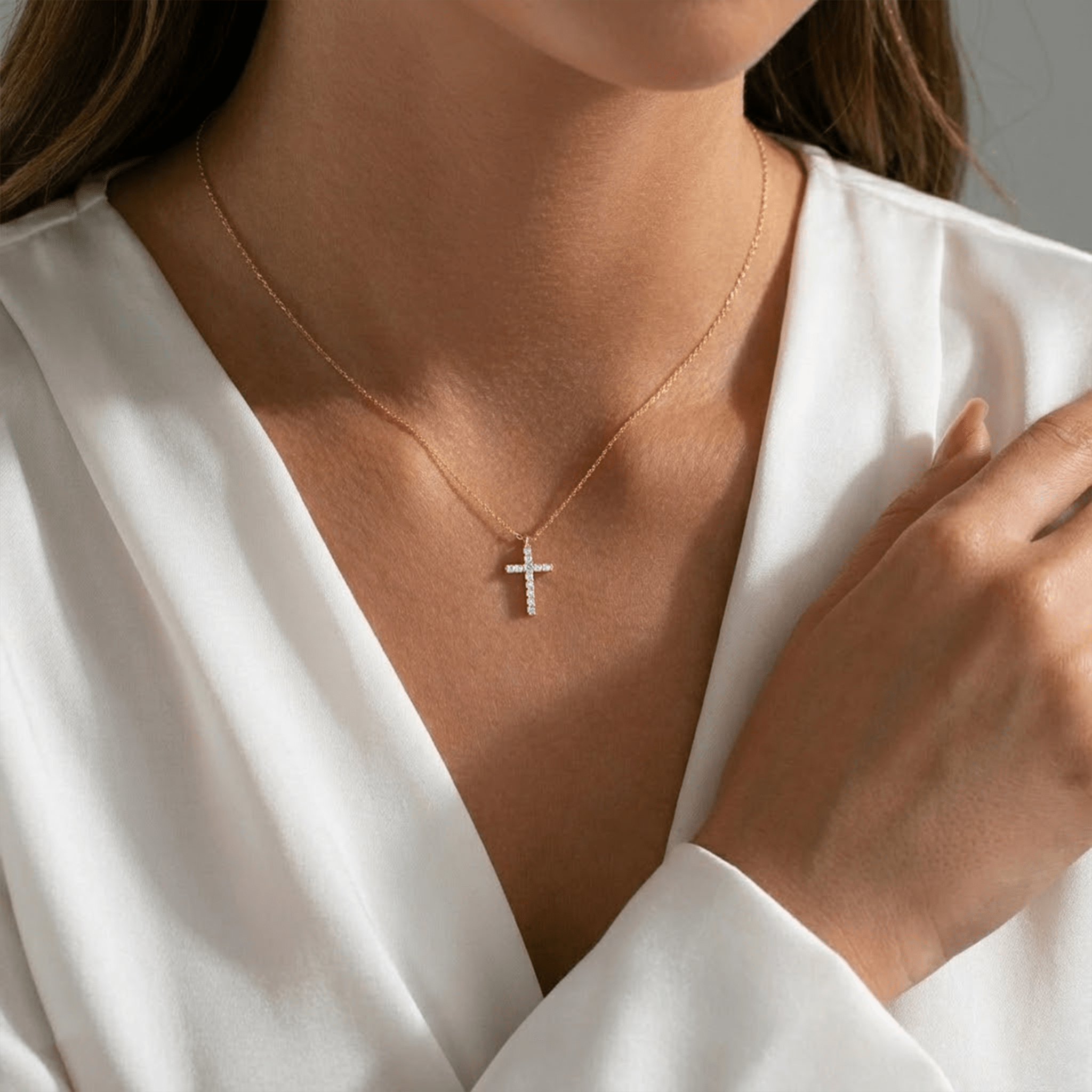 Person wearing a gold cross necklace with a white top